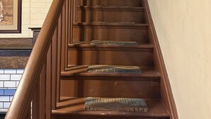 Un escalier en bois, doté d’une rampe, mène à un palier où est accrochée une image encadrée au mur.