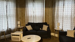 Un salon avec un canapé noir, deux rideaux à motifs, une table basse ronde et une petite table d’appoint avec une lampe.
