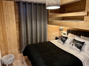Een slaapkamer met een stapelbed, een grijs gordijn, een klein krukje en een hangende lamp.