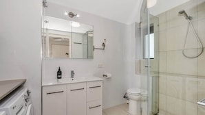 Un baño moderno con cabina de ducha de vidrio, un lavamanos blanco con espejo y un inodoro.
