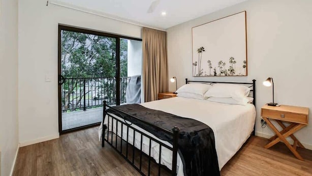 Un dormitorio con cama, ventilador de techo, mesita de noche, lámpara de noche y vistas al exterior a través de una puerta corrediza.