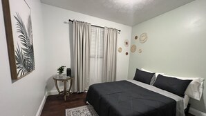 A bedroom with a large bed, a small table with a plant, and decorative wall art. - Modern & Convenient 3/2 Home (Lake City)