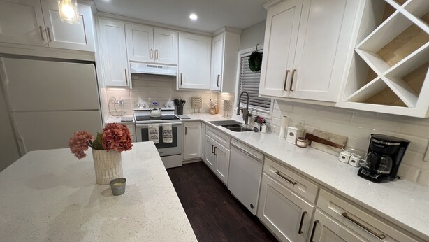 A modern kitchen with white cabinetry, a central island with a vase of flowers, and a coffee maker on the countertop. - Modern & Convenient 3/2 Home (Lake City)
