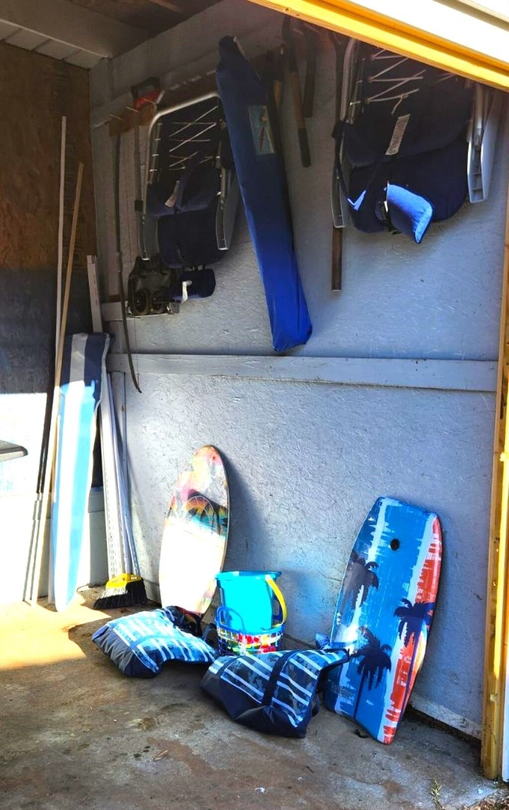 Garagem com pranchas de surf e outros equipamentos guardados em prateleiras e no chão.