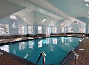 Une piscine intérieure à l’eau d’un bleu cristallin, entourée de fenêtres et dotée d’un sol carrelé.