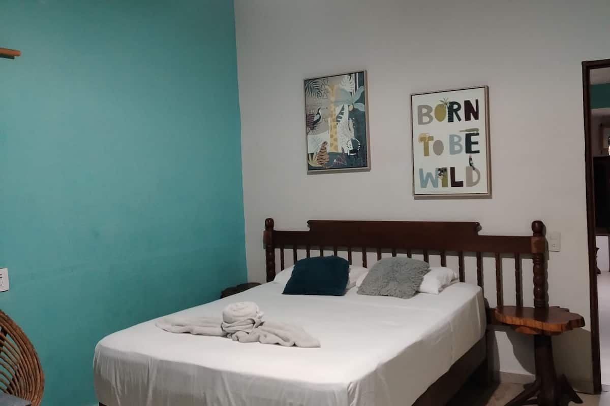 Une chambre à coucher comprenant un lit, un climatiseur fixé au mur, un luminaire suspendu et deux œuvres d’art murales.