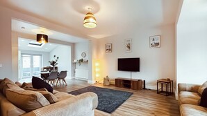 A modern living room with a sofa, a TV, and a dining area in the background.