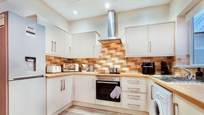 A modern kitchen with white cabinets, a stainless steel refrigerator, a built-in oven, a dishwasher, and a coffee maker.