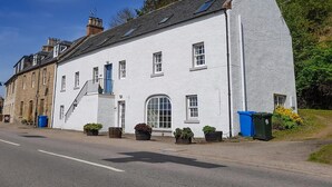 A white building with a steep roof, a blue door, and multiple windows. - 3 bedroom accommodation in Avoch, near Fortrose (Avoch, near Fortrose)