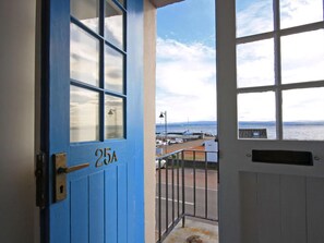 Puerta azul con el número 25A, que da a un balcón con vista al mar y barcos.