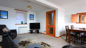 A living room with a sofa, TV, and a dining area with chairs and a table. - 3 bedroom accommodation in Avoch, near Fortrose (Avoch, near Fortrose)