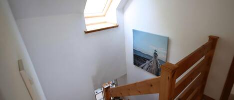 A staircase with wooden railings, a skylight, and a painting of a lighthouse.