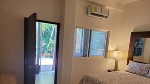 Un dormitorio con cama, ventana, equipo de aire acondicionado y puerta que da a un espacio exterior.