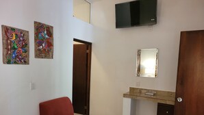 Un dormitorio con una silla roja, una cama con ropa de cama floral, un televisor y dos cuadros decorativos en la pared.