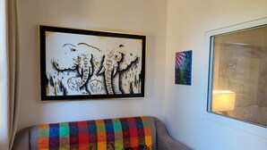Una sala de estar con un sofá gris, una manta colorida y dos cuadros enmarcados en la pared.