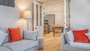 Een moderne woonkamer met twee grijze banken, een houten salontafel en een eethoek met een houten tafel en stoelen.
