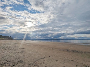 A beach with a wide sandy area, a calm body of water, and a cloudy sky.