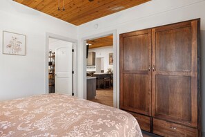 Een slaapkamer met een groot bed, een houten garderobe en een gang die leidt naar een keuken.
