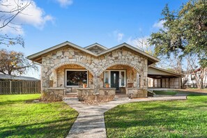 A stone house with a front porch, a garage, and a well-maintained lawn. - Place on Pecan | Close to Main in Cowboy Capital (Bandera)