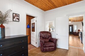 A room with a leather chair, a dresser, a vase with dried flowers, and a laundry sign on a door. - Place on Pecan | Close to Main in Cowboy Capital (Bandera)