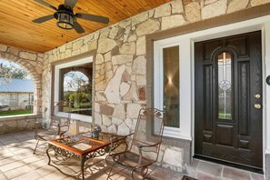 A covered patio with stone walls, a wooden ceiling, and a dark wooden door with a star-shaped window. - Place on Pecan | Close to Main in Cowboy Capital (Bandera)