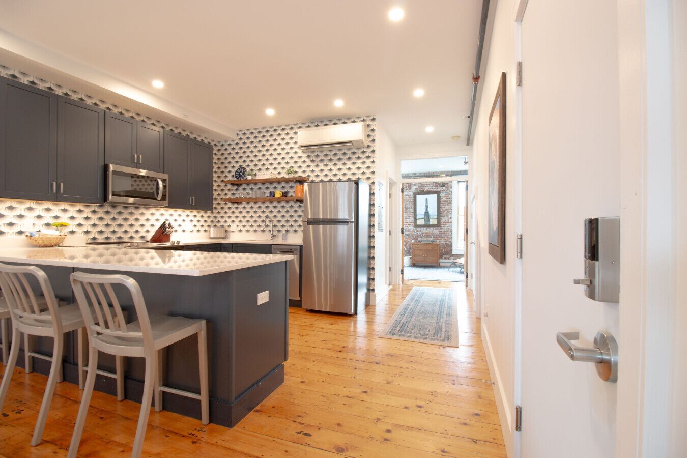 Una cocina moderna con armarios grises, un refrigerador de acero inoxidable y una isla central con taburetes de bar.