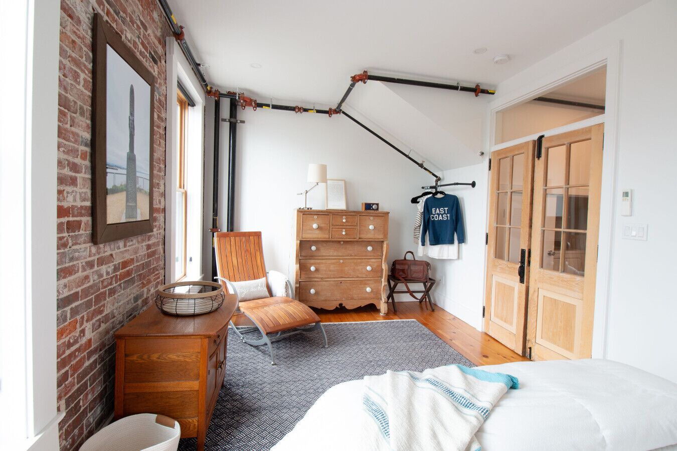 Ein Schlafzimmer mit Backsteinwand, einem hölzernen Schminktisch, einem Stuhl, einem Bett, einem Kleiderständer und einer Tür.