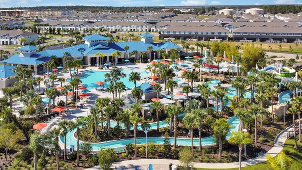 Un resort con varias piscinas, palmeras y un edificio grande con techos azules.