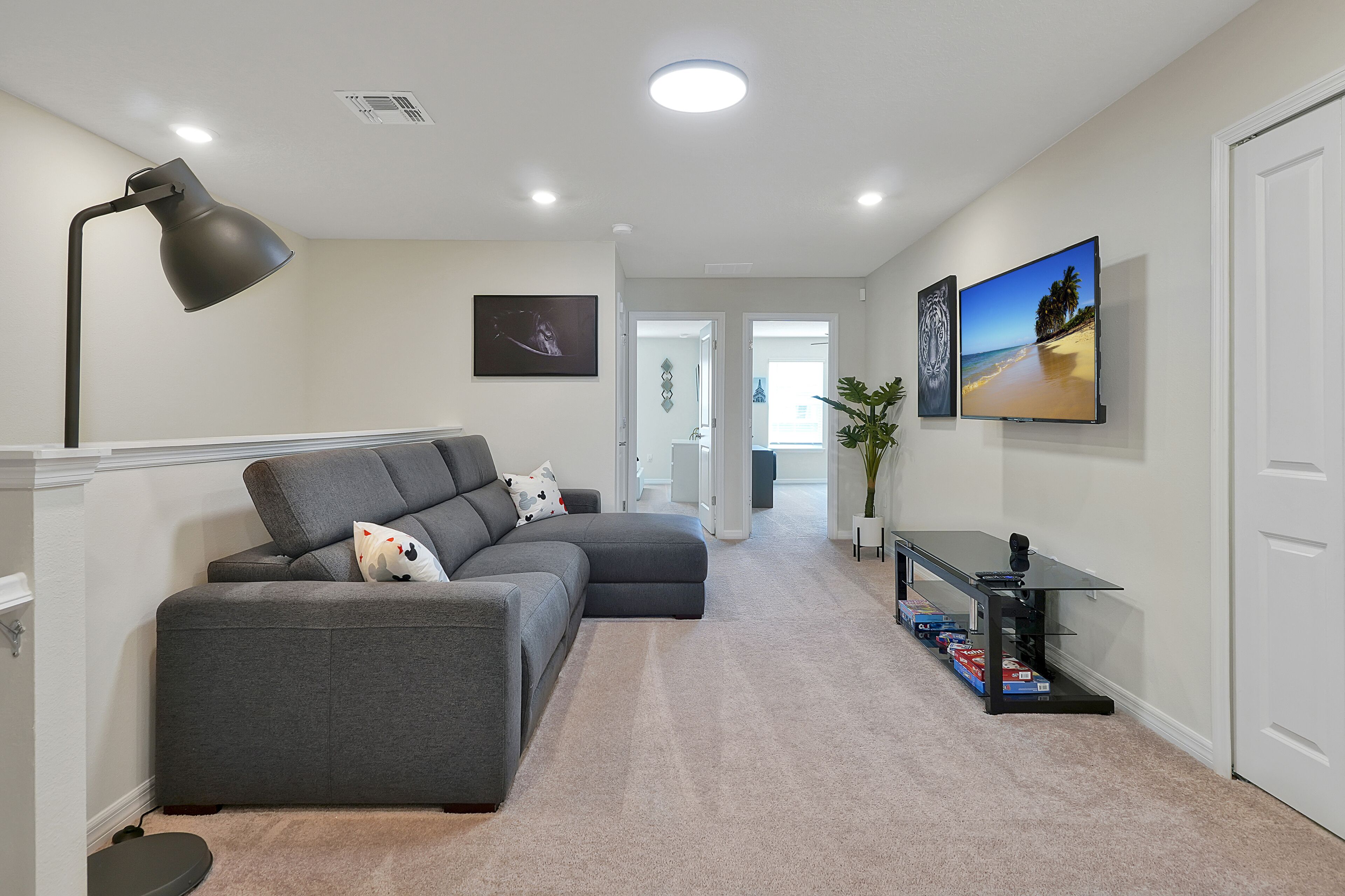 A modern living room with a grey sectional sofa, a black floor lamp, and a flat-screen TV mounted on the wall.