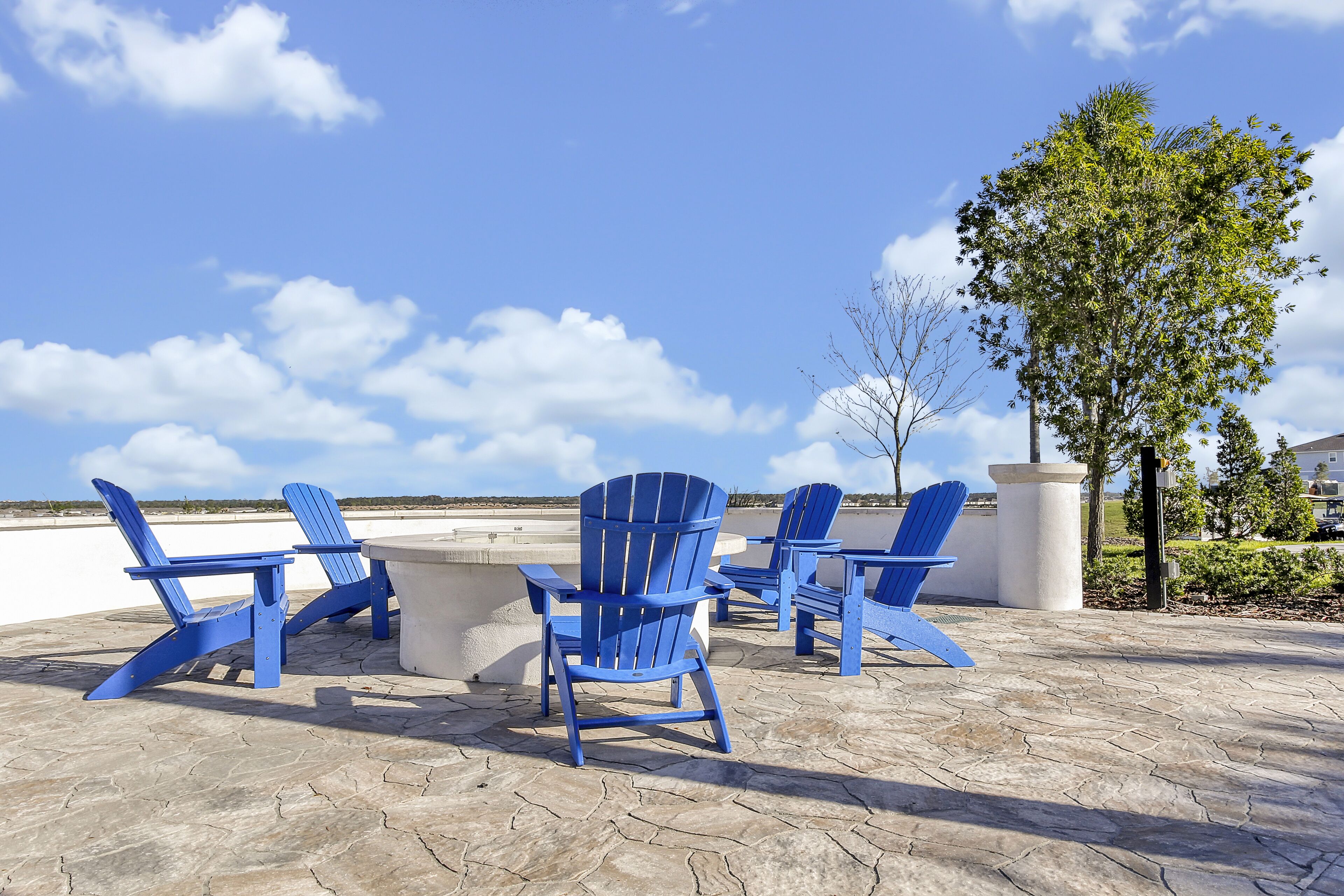 A patio area with blue Adirondack chairs and a concrete table.