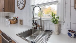 Una cocina con un lavamanos de acero inoxidable, un reloj en la pared y una ventana con persianas.