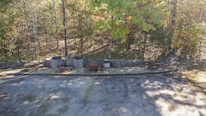 Un muret en pierre avec un banc et un espace barbecue, le tout situé dans un cadre boisé.