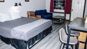 A room with a bed, a blue sofa, a dining table with chairs, and a window with curtains. - Renovated King Kitchenette (Branson)