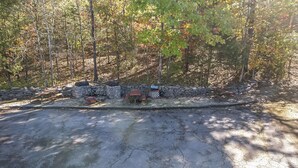 A stone wall with a bench and a grill area in a forested setting. - Renovated King Kitchenette (Branson)