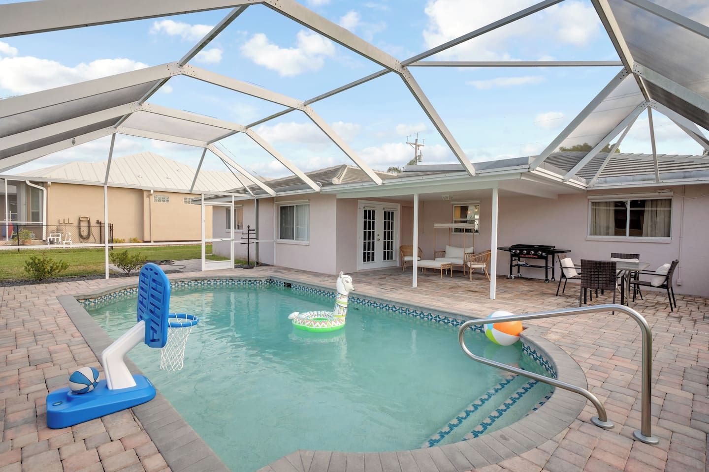 A covered swimming pool with a slide, lounge chairs, and a barbecue area.