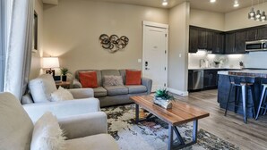 A modern living room with a sofa, a coffee table, and a kitchen area with a microwave and bar stools.