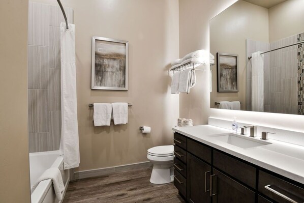 A modern bathroom with a white toilet, wooden flooring, a large mirror, and dark wooden cabinets.