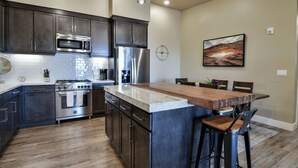 A modern kitchen with dark cabinets, stainless steel appliances, a wooden island, and a dining area with bar stools.
