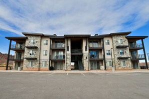 A multi-story building with a central entrance, balconies, and a parking lot in front.