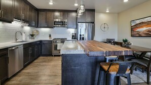 A modern kitchen with dark wood cabinets, stainless steel appliances, and a central island with bar stools. - Sage Creek Desert Escape C2 - Luxury Pool & HotTub (Moab)