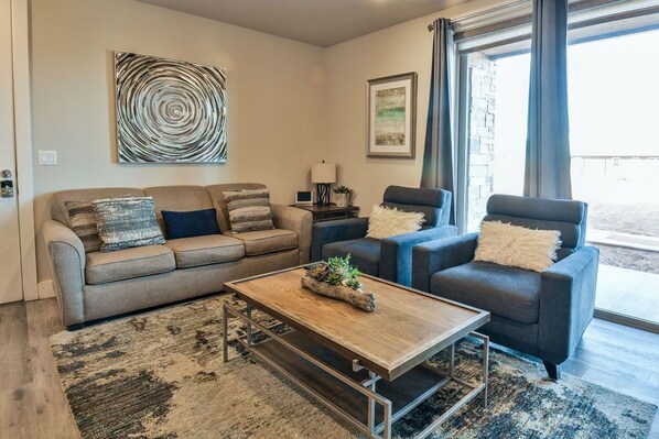 A modern living room with a beige sofa, a blue armchair, and a wooden coffee table.
