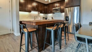 A modern kitchen with dark wooden cabinets, stainless steel appliances, and a central island with bar stools. - Moab Arches C4 "Sage Creek" - Heated Pool-Hot Tubs (Moab)