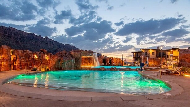 A pool with a waterfall feature, surrounded by rock formations and a mountain backdrop. - SageCreek C5 - Best Pool & Red Rock View - Hot Tub (Moab)