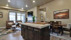 A modern kitchen with dark cabinetry, a central island, and a dining area with wooden chairs and a table. - SageCreek C5 - Best Pool & Red Rock View - Hot Tub (Moab)