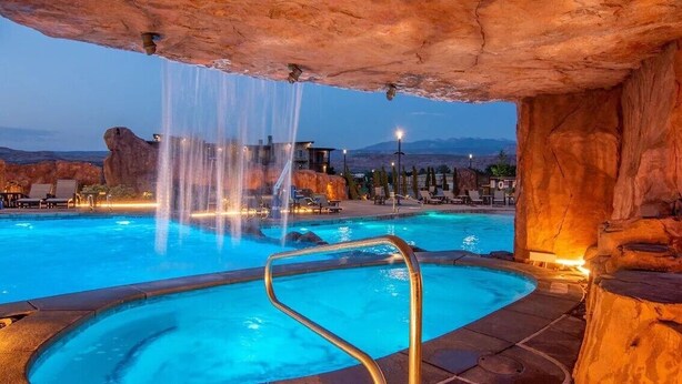 A pool with a waterfall feature, surrounded by rock formations and lounge chairs. - Sage Creek Resort - 3BR Condo - C6 | Pool - HotTub (Moab)