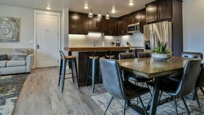 A modern kitchen with dark wood cabinets, a central island with bar stools, a dining table with chairs, and a refrigerator. - SageCreek Moab Resort "C8" - Heated Pool - Hot Tub (Moab)