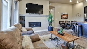 Una sala de estar moderna con chimenea, un televisor de pantalla plana grande, un sofá y un comedor con sillas y barra.