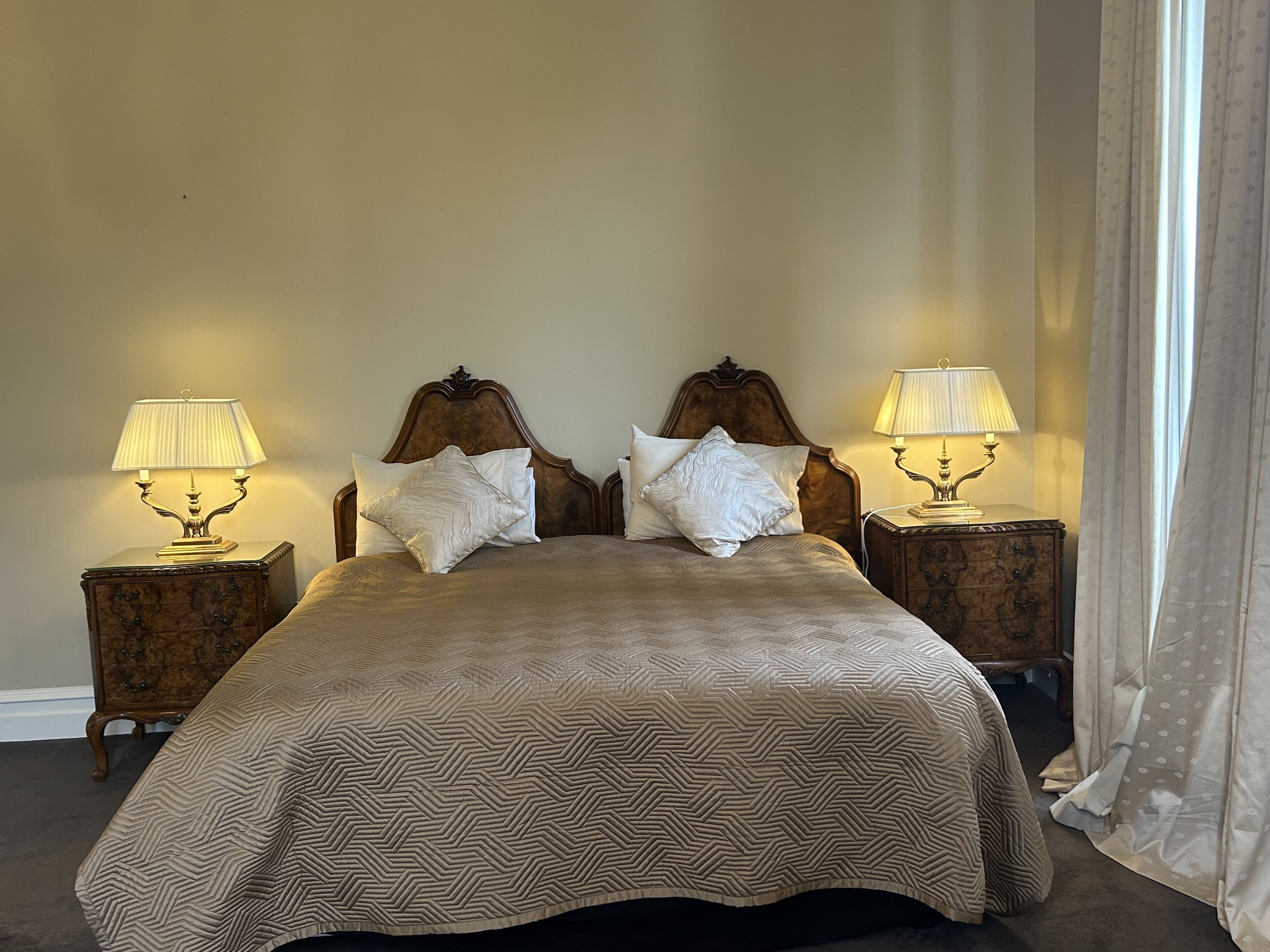 Ein Doppelbett mit gemustertem Bettbezug, zwei Nachttische mit Lampen und ein Holz-Kopfstück.