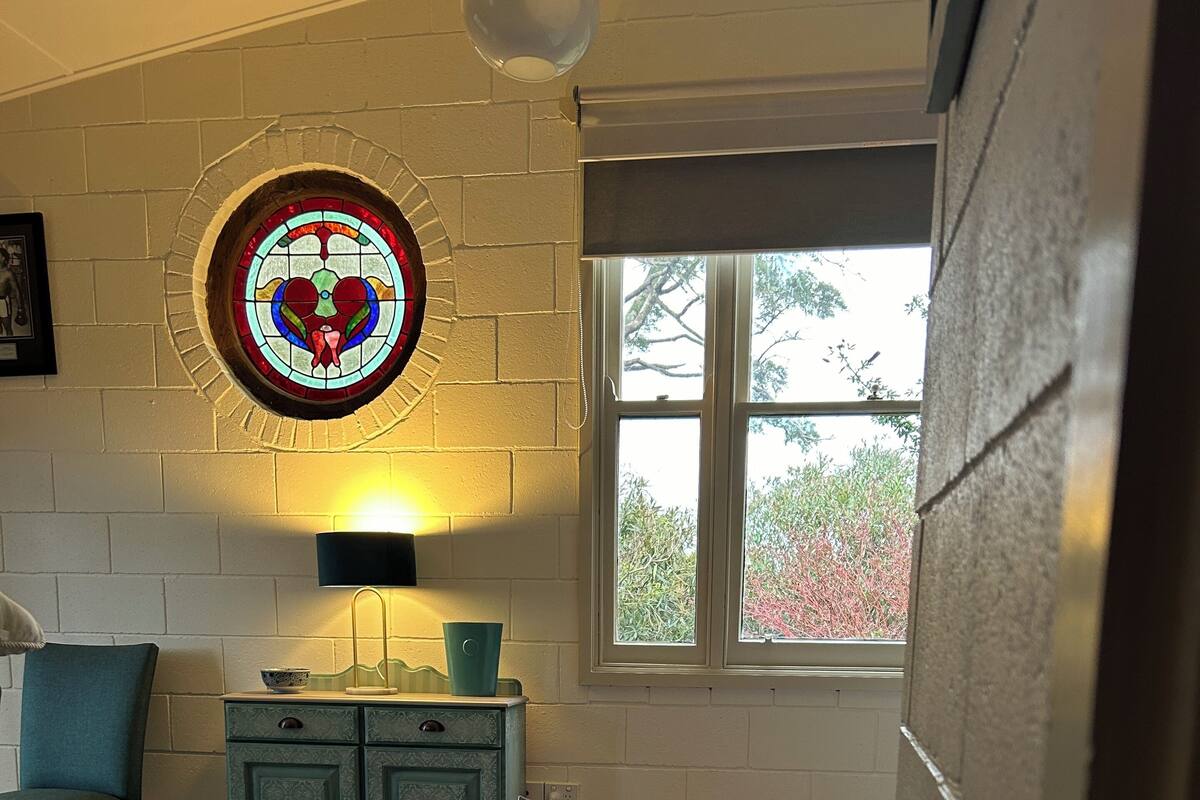 A cozy room with a wooden floor, a blue rug, a teal chair, a cabinet, and a stained glass window.