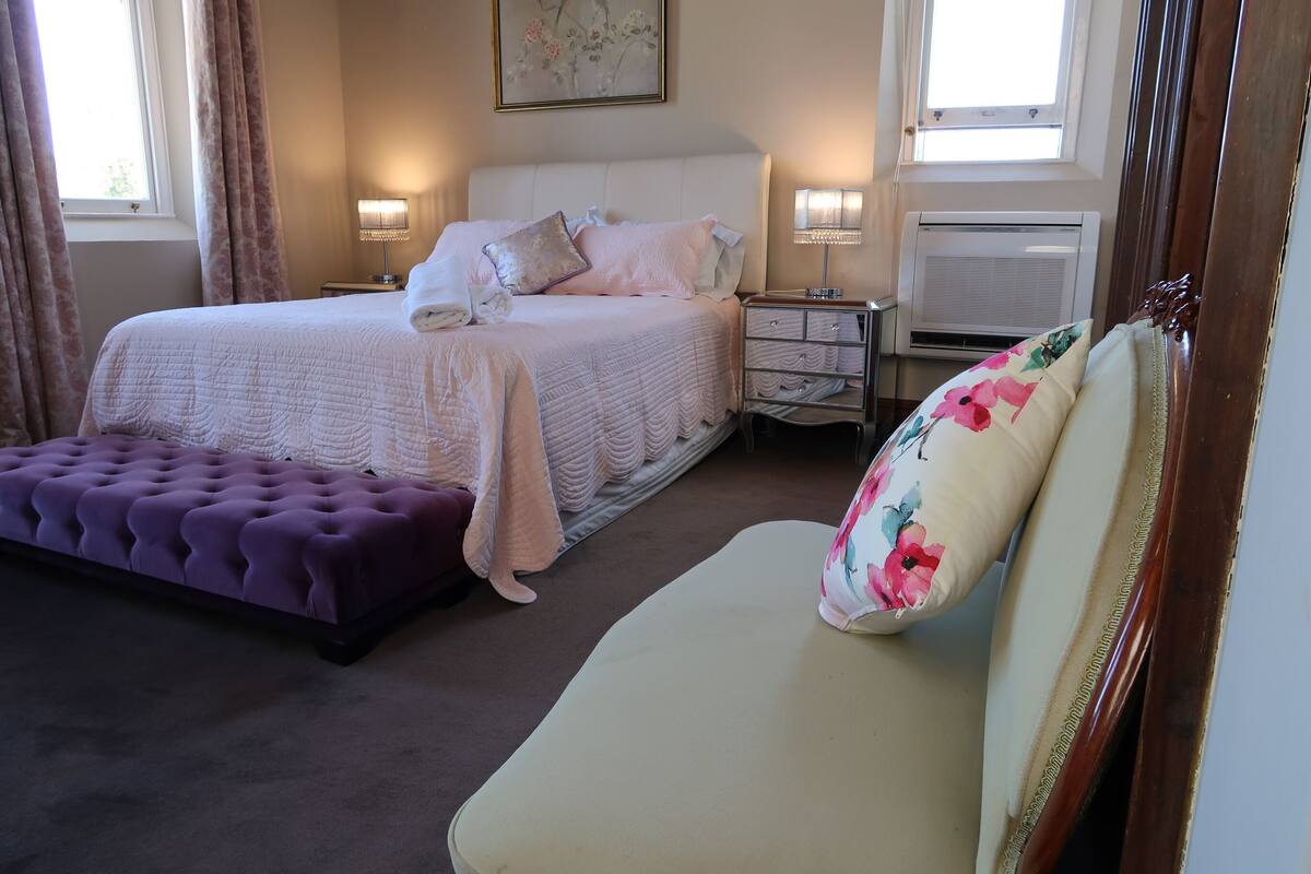 A bedroom with a bed, bedside tables, a lamp, a radiator, a window, and a sofa.